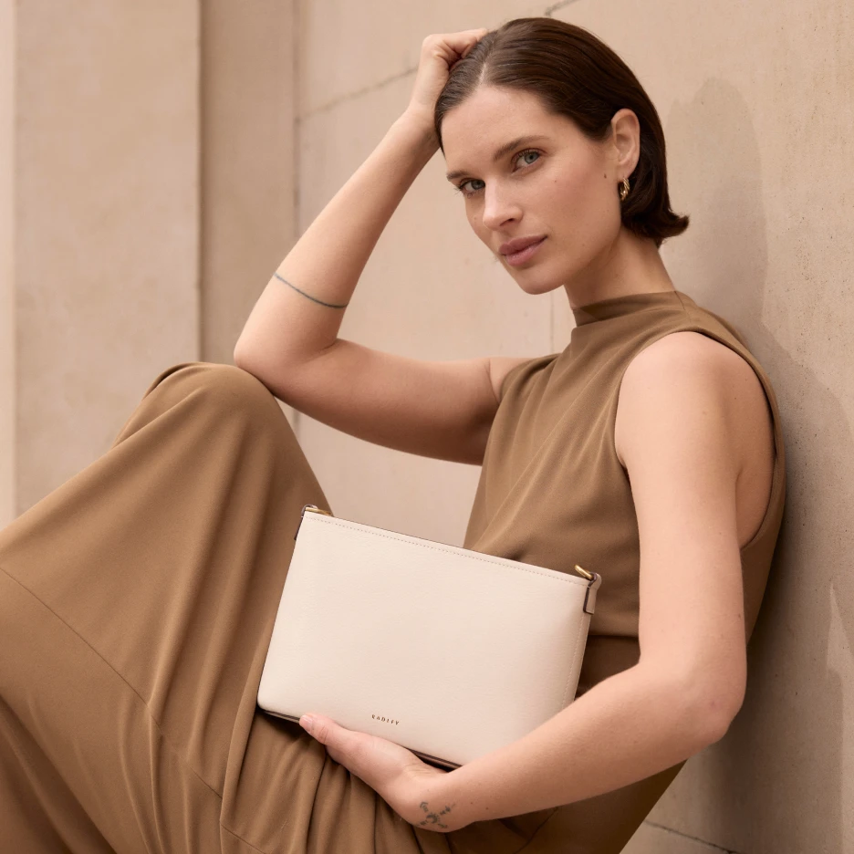 Fashion model posing with minimalist beige handbag against neutral background in editorial lifestyle photoshoot