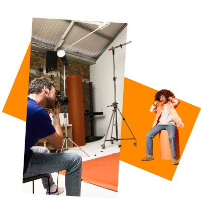 Photographer taking a studio portrait of a model posing against an orange backdrop during a professional photoshoot.
