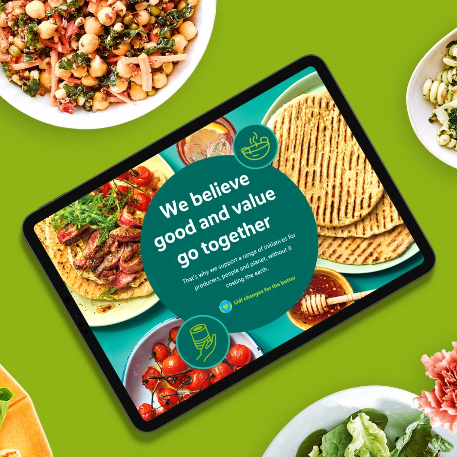 Tablet displaying food brand sustainability webpage surrounded by fresh dishes and ingredients